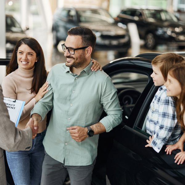 happy parents shaking hands with a car salesperson in a showroom.